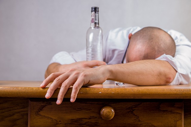 A man passed out at a table with an almost empty bottle of alcohol sitting next to him.