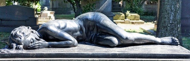 A grave marker carving of a young woman lying on her side, covering her face. She looks as if she is grieving.