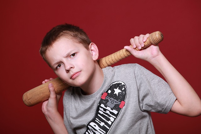 A young boy standing menacingly and holding a bat over his shoulders.