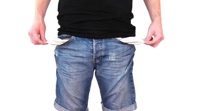 A man standing with his pockets turned out, symbolizing a lack of money