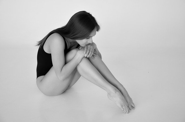 A young gymnast sitting on the ground with her knees together, looking sad and thoughtful