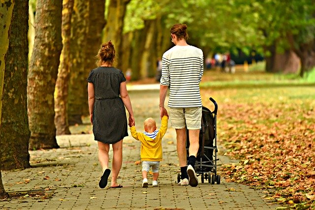 A couple walking in the autumn, holding hands with a toddler who is walking between them.